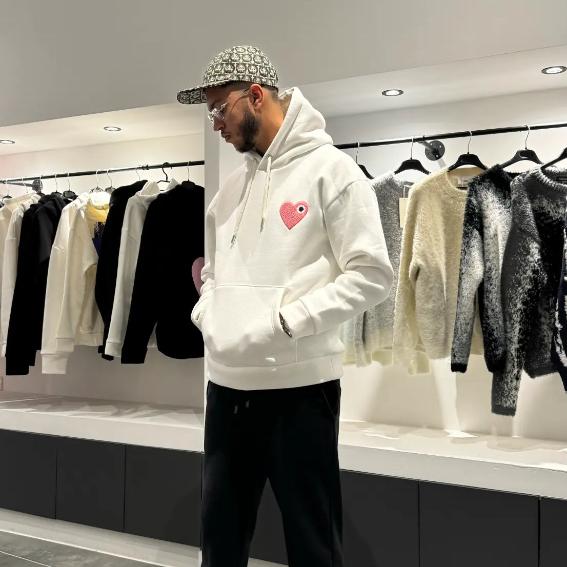 Modèle debout arborant la shape et la coupe classique du pull ADJ blanc avec le coeur rose pour un outfit urbain impeccable.