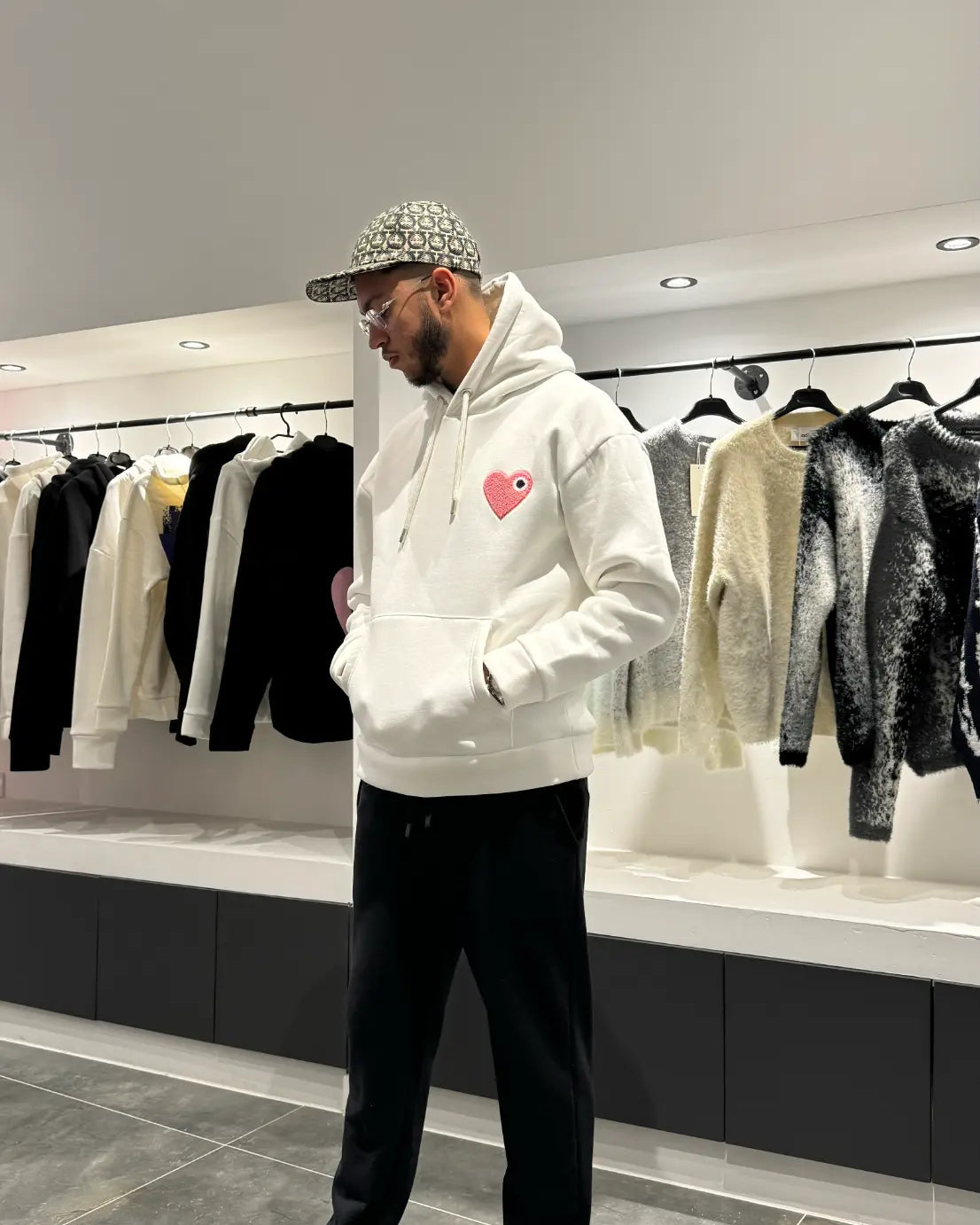 Modèle debout arborant la shape et la coupe classique du pull ADJ blanc avec le coeur rose pour un outfit urbain impeccable.