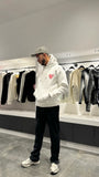 Modèle debout arborant la shape et la coupe classique du pull ADJ blanc avec le coeur rose pour un outfit urbain impeccable.