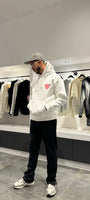 Modèle debout arborant la shape et la coupe classique du pull ADJ blanc avec le coeur rose pour un outfit urbain impeccable.