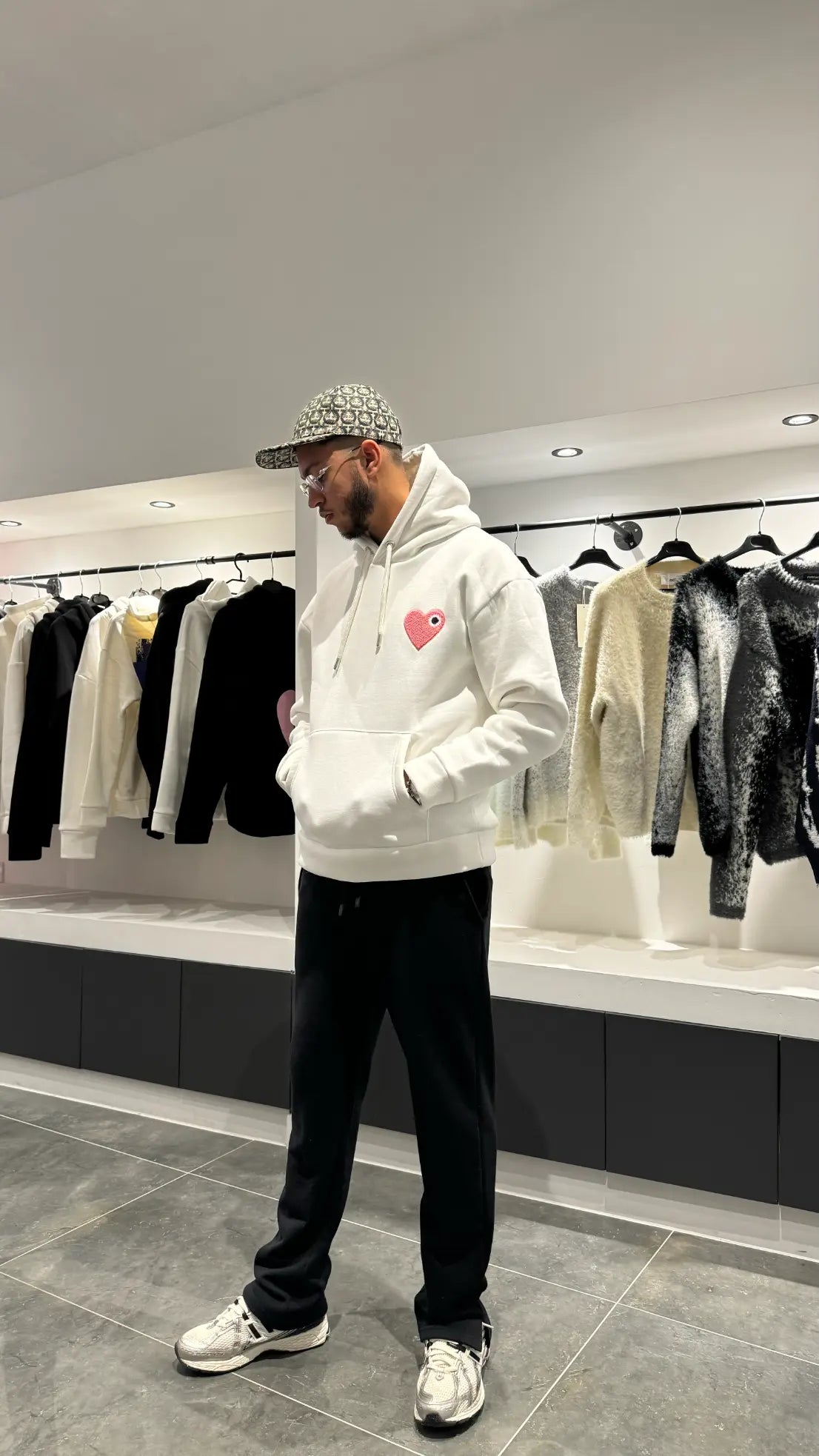 Modèle debout arborant la shape et la coupe classique du pull ADJ blanc avec le coeur rose pour un outfit urbain impeccable.
