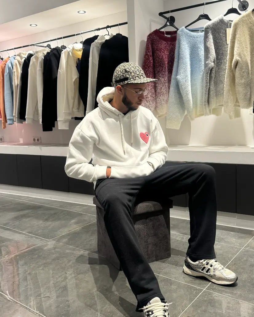 Modèle assis avec le pull ADJ blanc et son cœur rose brodé pour un look streetwear décontracté et clean.