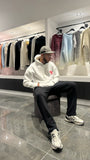 Modèle assis avec le pull ADJ blanc et son cœur rose brodé pour un look streetwear décontracté et clean.