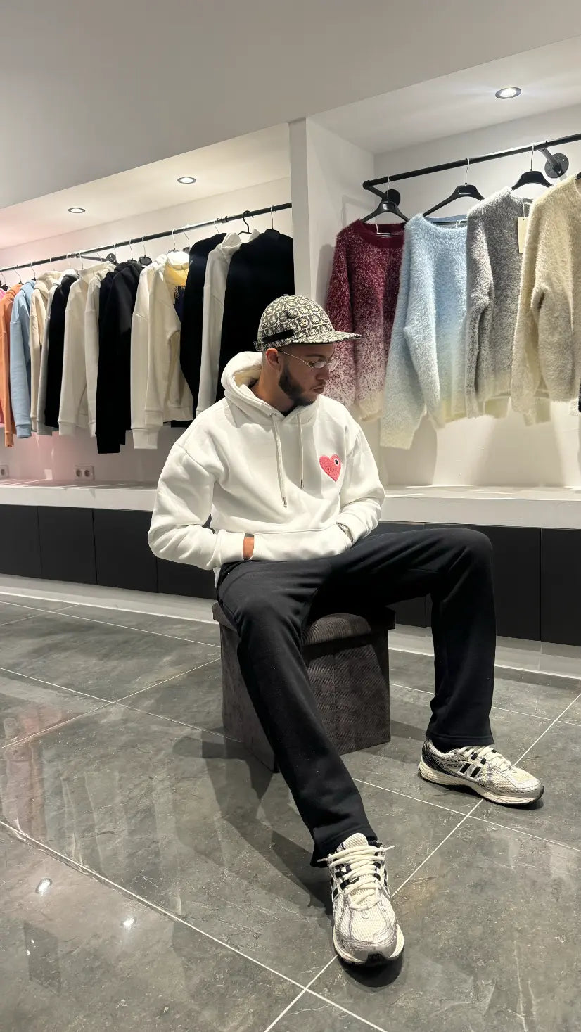 Modèle assis avec le pull ADJ blanc et son cœur rose brodé pour un look streetwear décontracté et clean.
