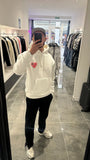 Selfie-look du pull à capuche ADJ blanc devant le miroir mettant en valeur le cœur rose en éponge et les détails.