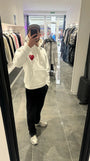 Selfie-look reflétant les détails du cœur rouge brodé en relief sur le pull à capuche ADJ blanc.