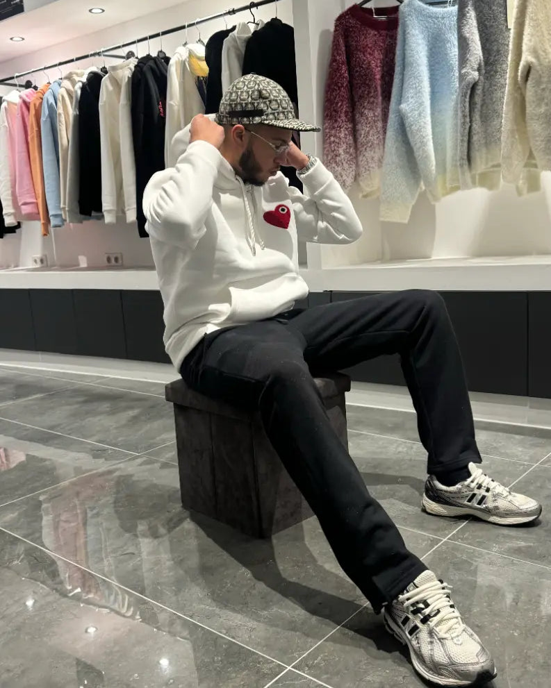 Modèle assis avec le pull ADJ blanc au cœur rouge pour un rendu décontracté et une attitude street.