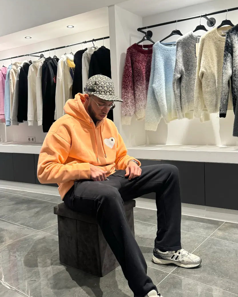 Modèle assis avec le pull ADJ orange clair pour une attitude décontractée mettant en avant le cœur blanc brodé.