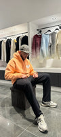 Modèle assis avec le pull ADJ orange clair pour une attitude décontractée mettant en avant le cœur blanc brodé.