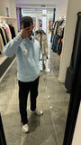 Modèle assis avec le pull ADJ bleu clair et son cœur blanc brodé pour un look streetwear décontracté.