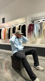Modèle assis avec le pull ADJ bleu clair et son cœur blanc brodé pour un look streetwear décontracté.