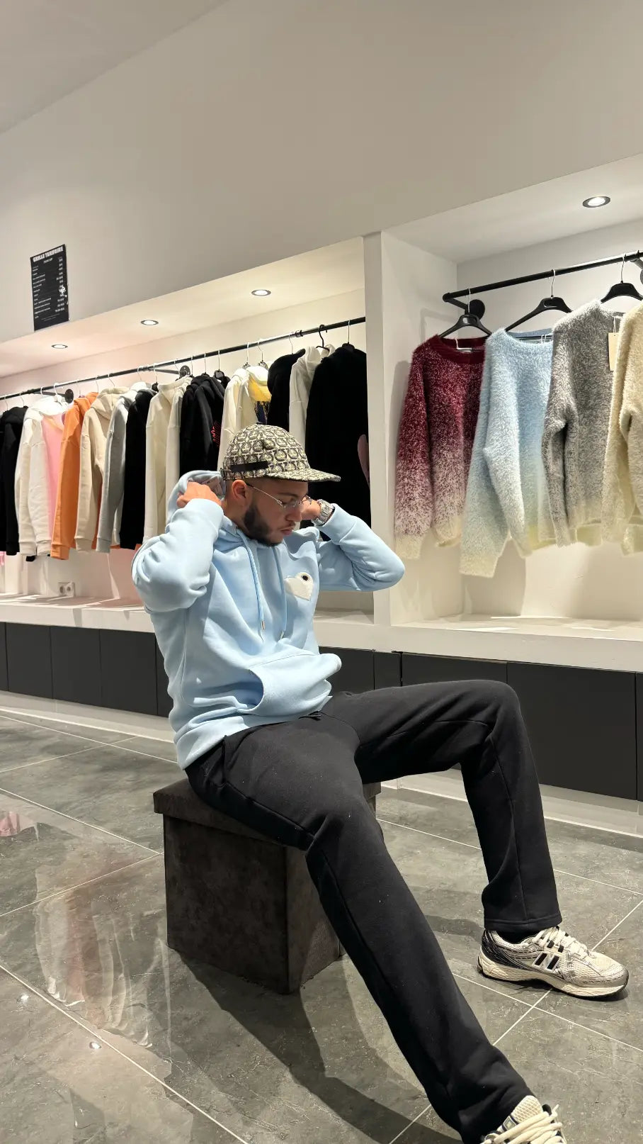 Modèle assis avec le pull ADJ bleu clair et son cœur blanc brodé pour un look streetwear décontracté.