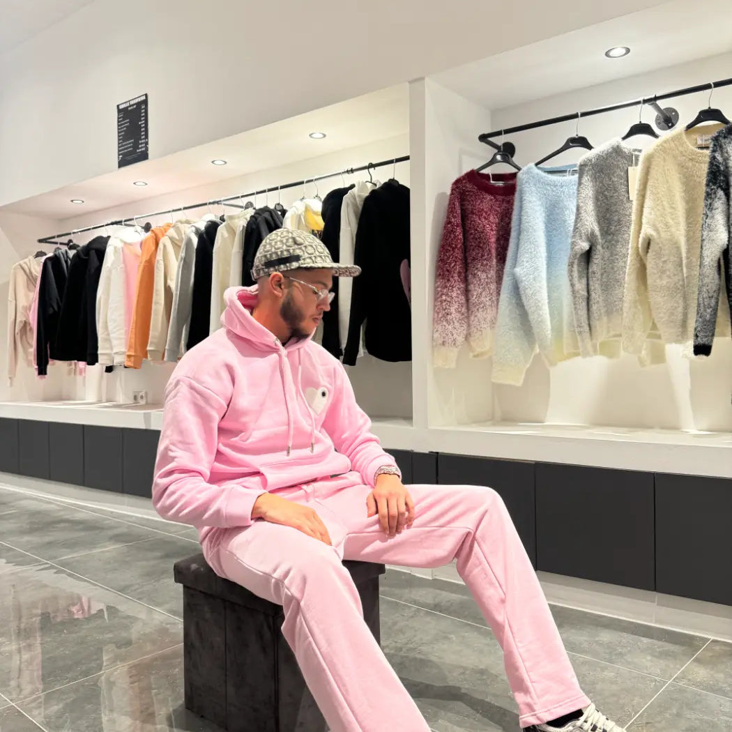 Modèle assis avec le pull ADJ rose et son cœur blanc brodé pour une pose décontractée et stylée.