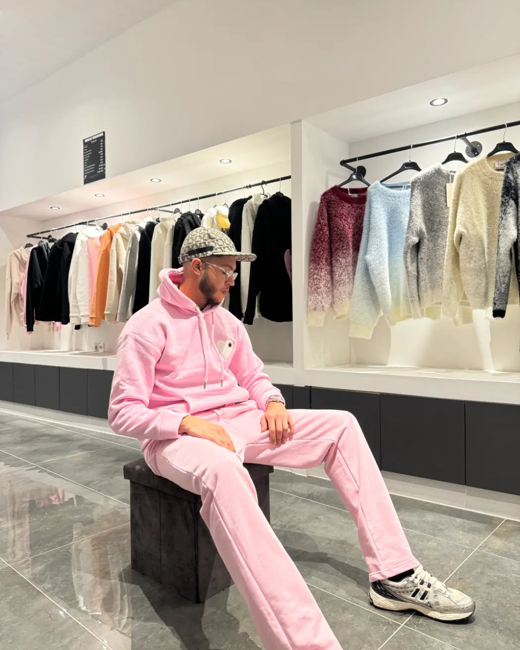 Modèle assis avec le pull ADJ rose et son cœur blanc brodé pour une pose décontractée et stylée.