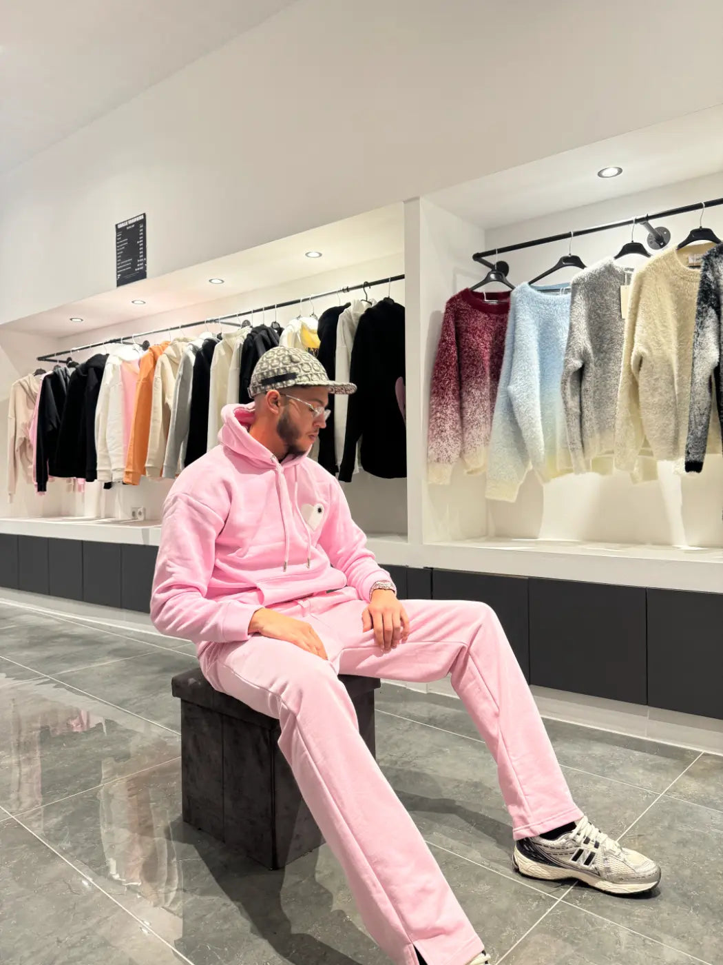 Modèle assis avec le pull ADJ rose et son cœur blanc brodé pour une pose décontractée et stylée.