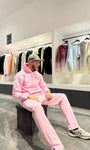 Modèle assis avec le pull ADJ rose et son cœur blanc brodé pour une pose décontractée et stylée.