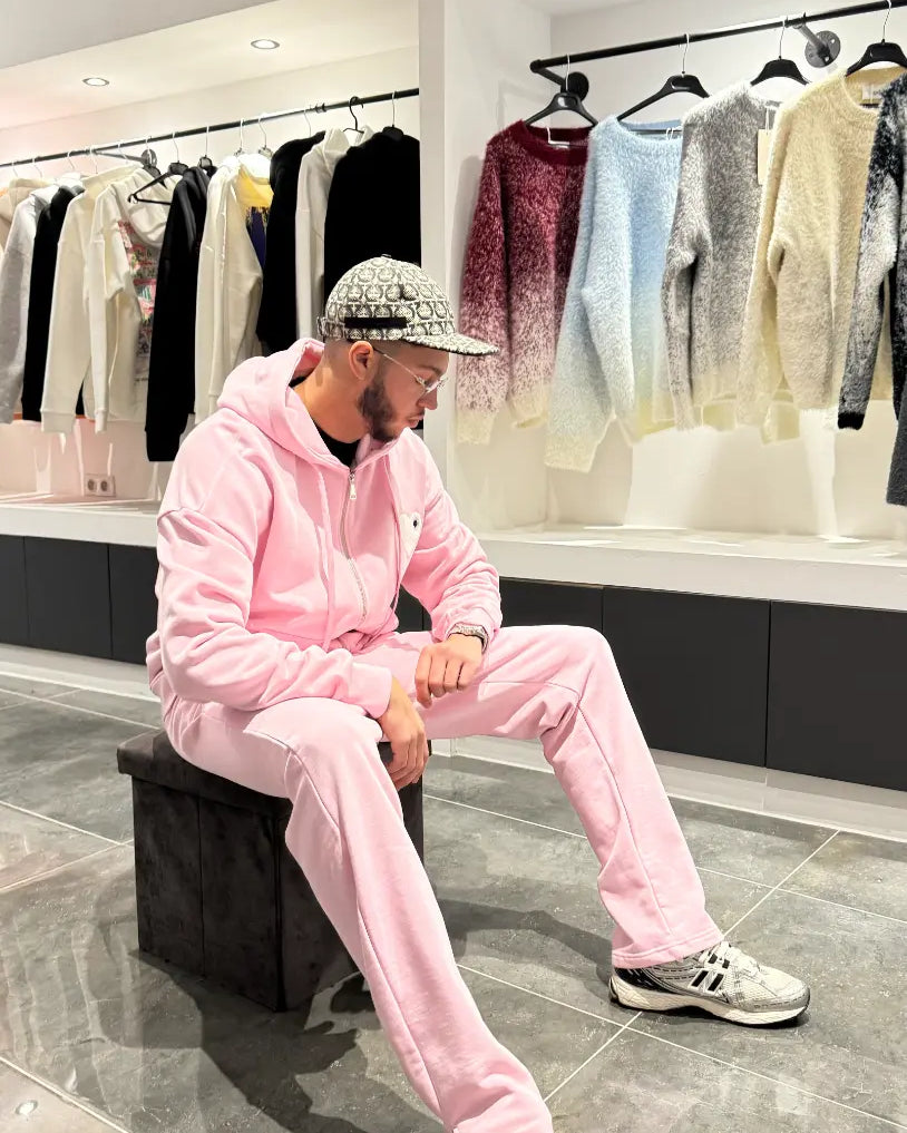 Modèle assis portant le zipper hoodie ADJ rose avec son cœur blanc brodé pour un look décontracté.
