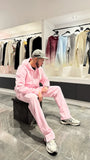 Modèle assis portant le zipper hoodie ADJ rose avec son cœur blanc brodé pour un look décontracté.