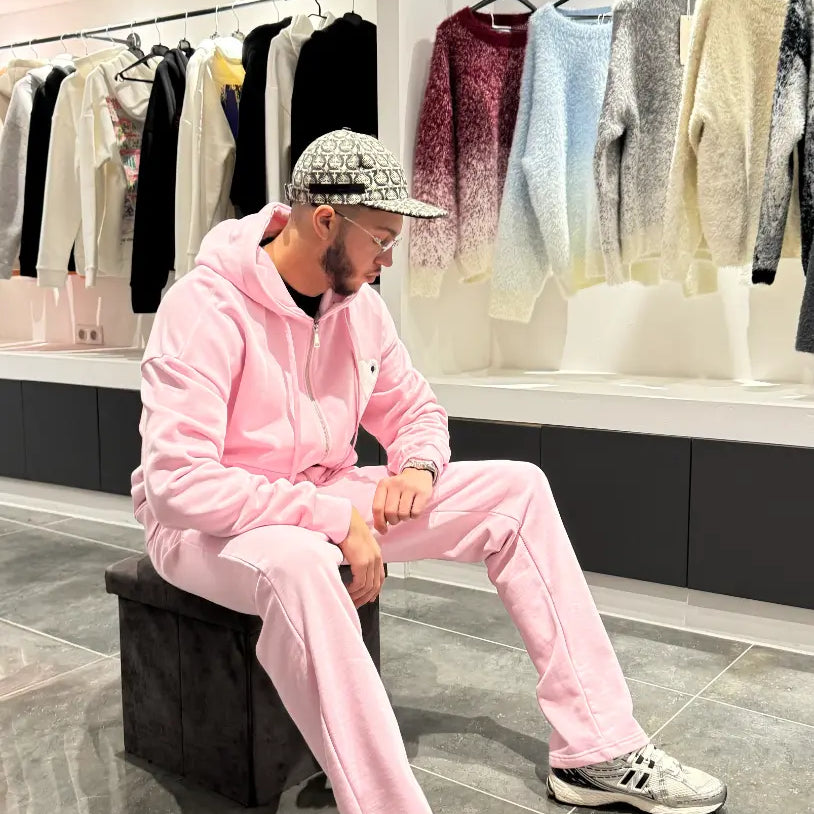 Modèle assis portant le zipper hoodie ADJ rose avec son cœur blanc brodé pour un look décontracté.