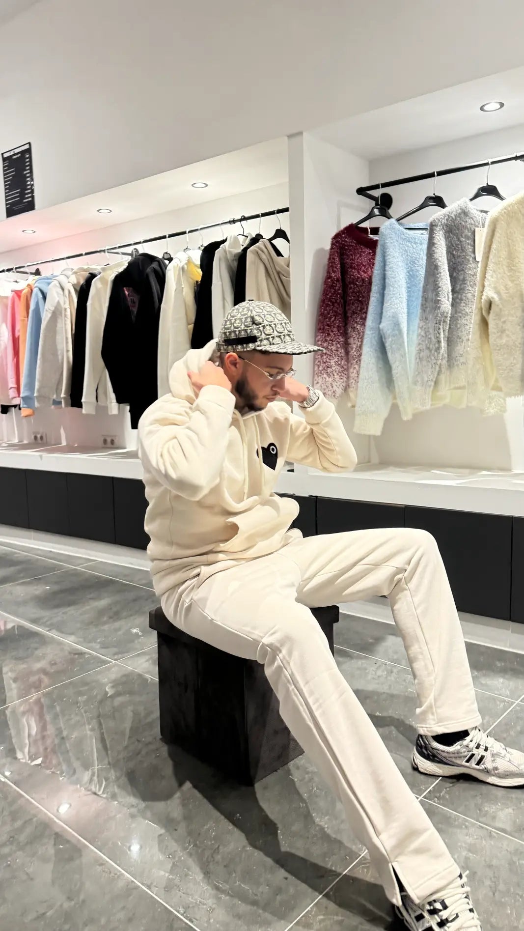 Modèle assis portant le pull ADJ beige avec cœur noir brodé pour un look streetwear posé et clean.