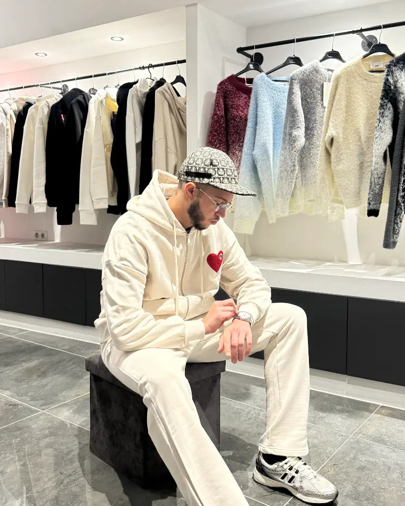 Pose décontractée du modèle assis portant le gilet ADJ beige avec son cœur rouge brodé.