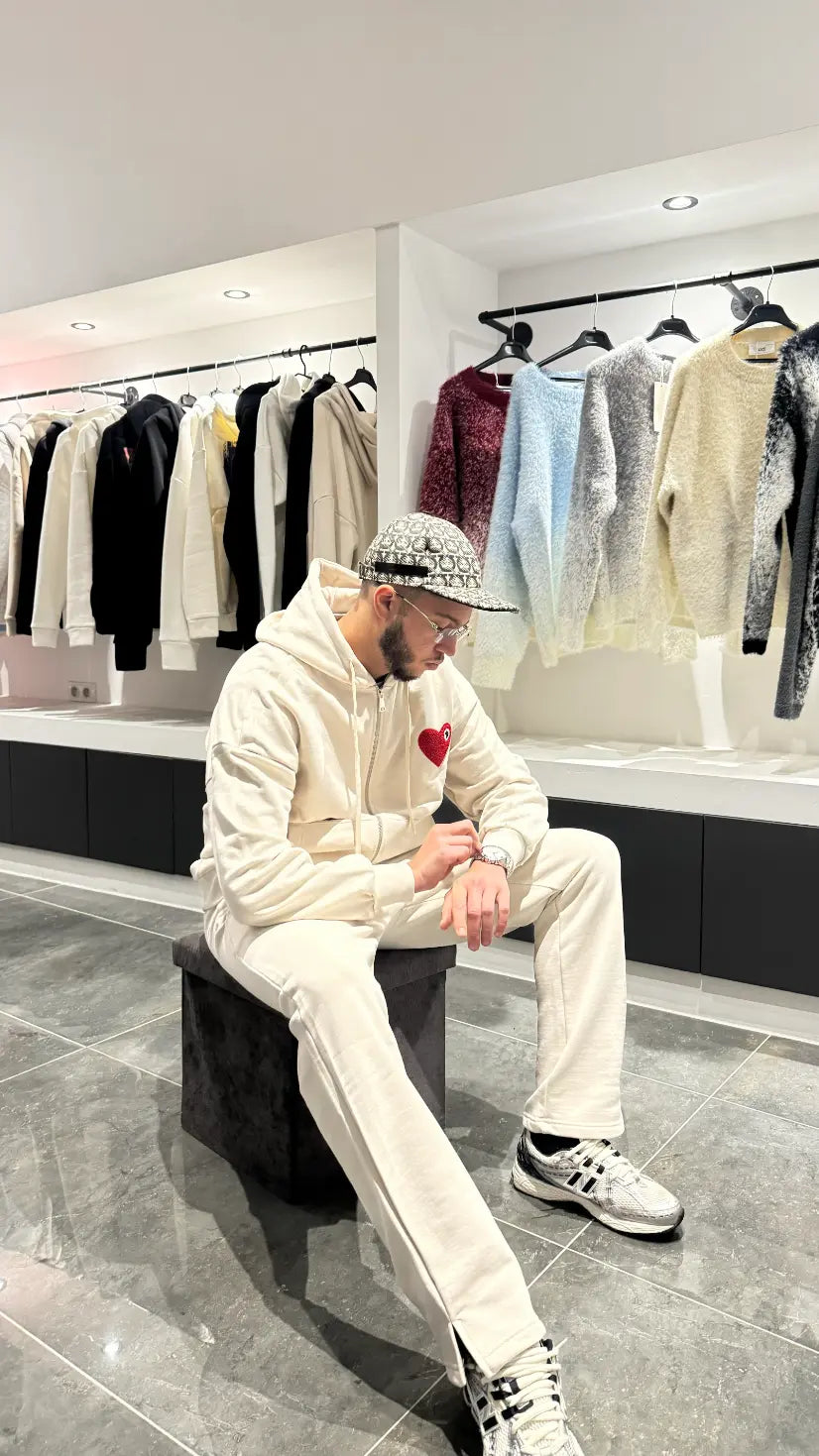 Pose décontractée du modèle assis portant le gilet ADJ beige avec son cœur rouge brodé.