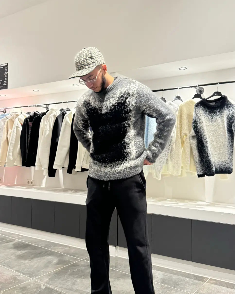 Silhouette sombre et structurée du modèle debout avec le pull premium noir et gris.