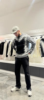 Silhouette sombre et structurée du modèle debout avec le pull premium noir et gris.
