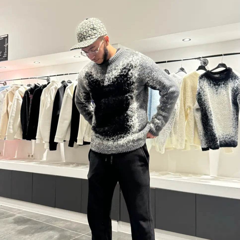 Silhouette sombre et structurée du modèle debout avec le pull premium noir et gris.