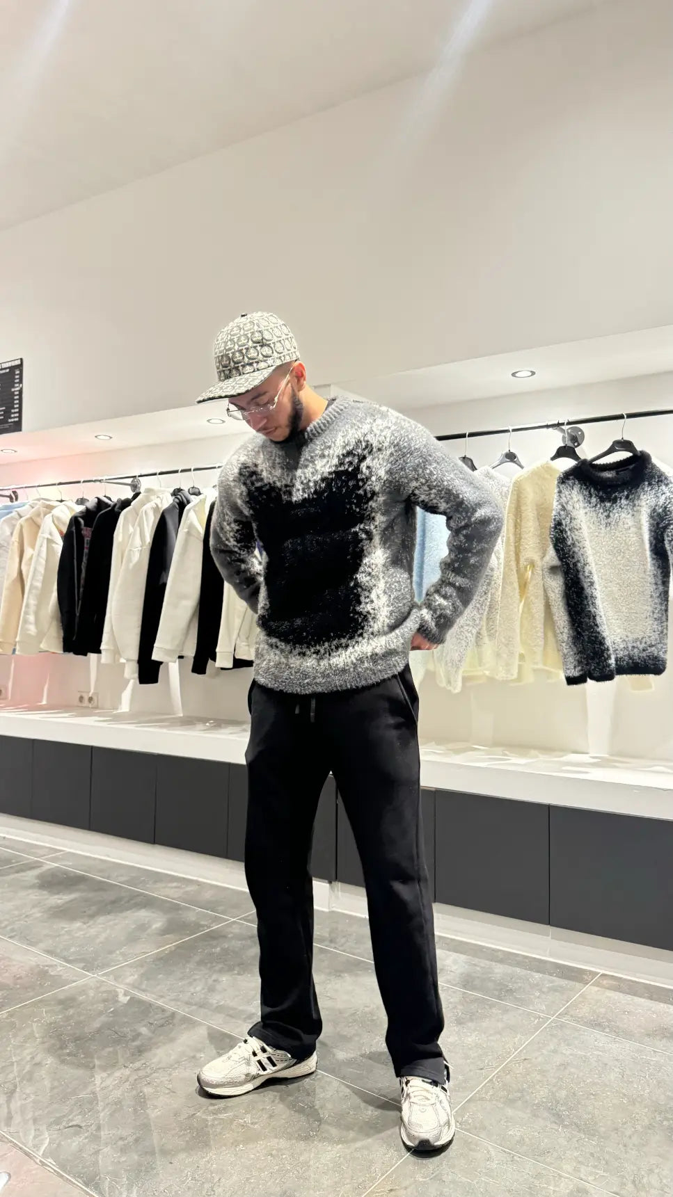 Silhouette sombre et structurée du modèle debout avec le pull premium noir et gris.