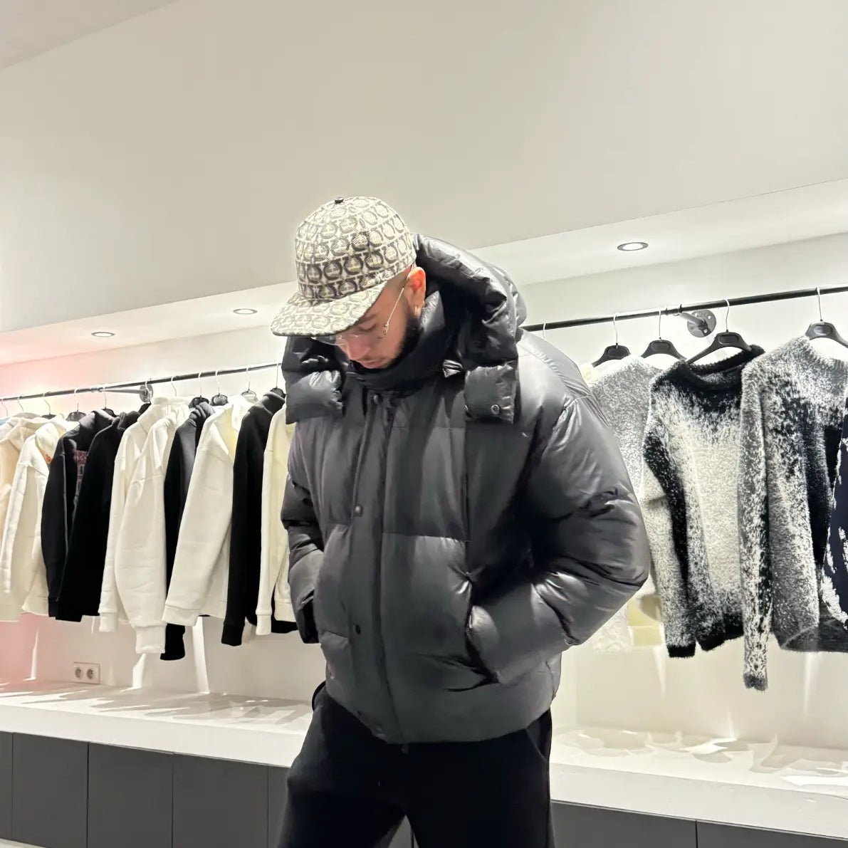 Silhouette complète montrant la doudoune noire brillante avec sa capuche, reflétant la lumière pour un look street haut de gamme.