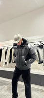 Silhouette complète montrant la doudoune noire brillante avec sa capuche, reflétant la lumière pour un look street haut de gamme.