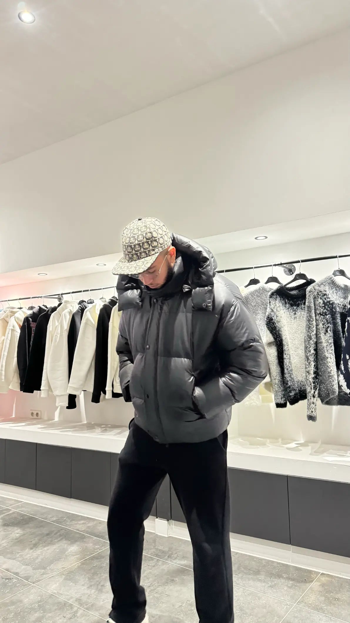 Silhouette complète montrant la doudoune noire brillante avec sa capuche, reflétant la lumière pour un look street haut de gamme.