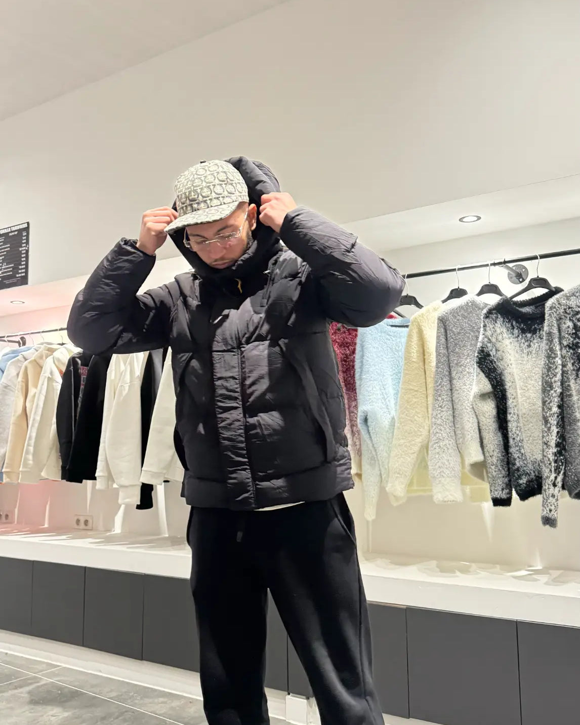 Silhouette complète montrant la doudoune noire technique fermée, mettant en avant les bandes cousues aux épaules.