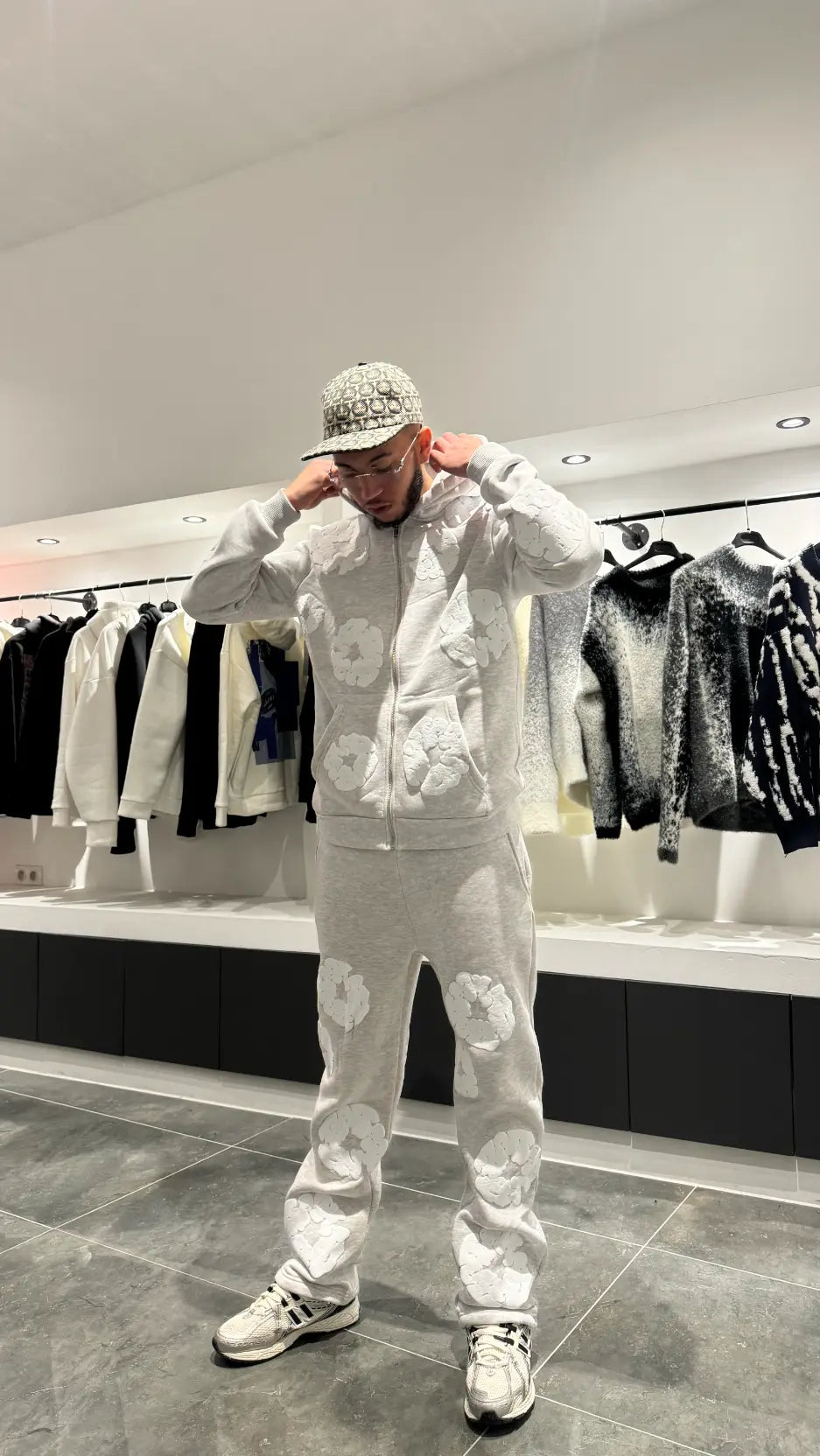 Vue de face montrant la coupe ajustée du pantalon et le hoodie zippé ouvert, révélant un style décontracté.