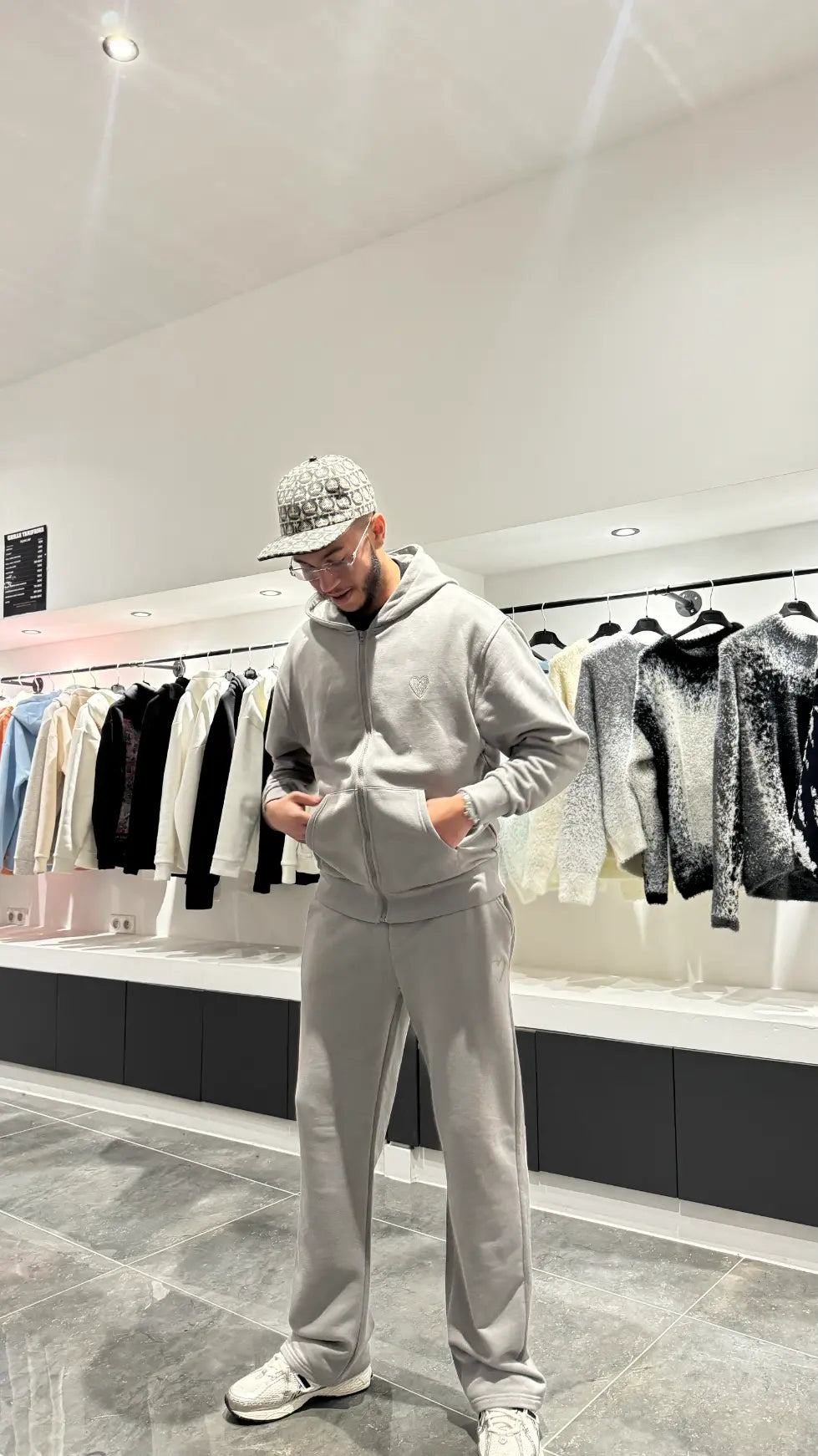 Ensemble complet gris composé d'une veste zippée à capuche et d'un jogging, mettant en avant le petit logo cœur brodé sur la poitrine.