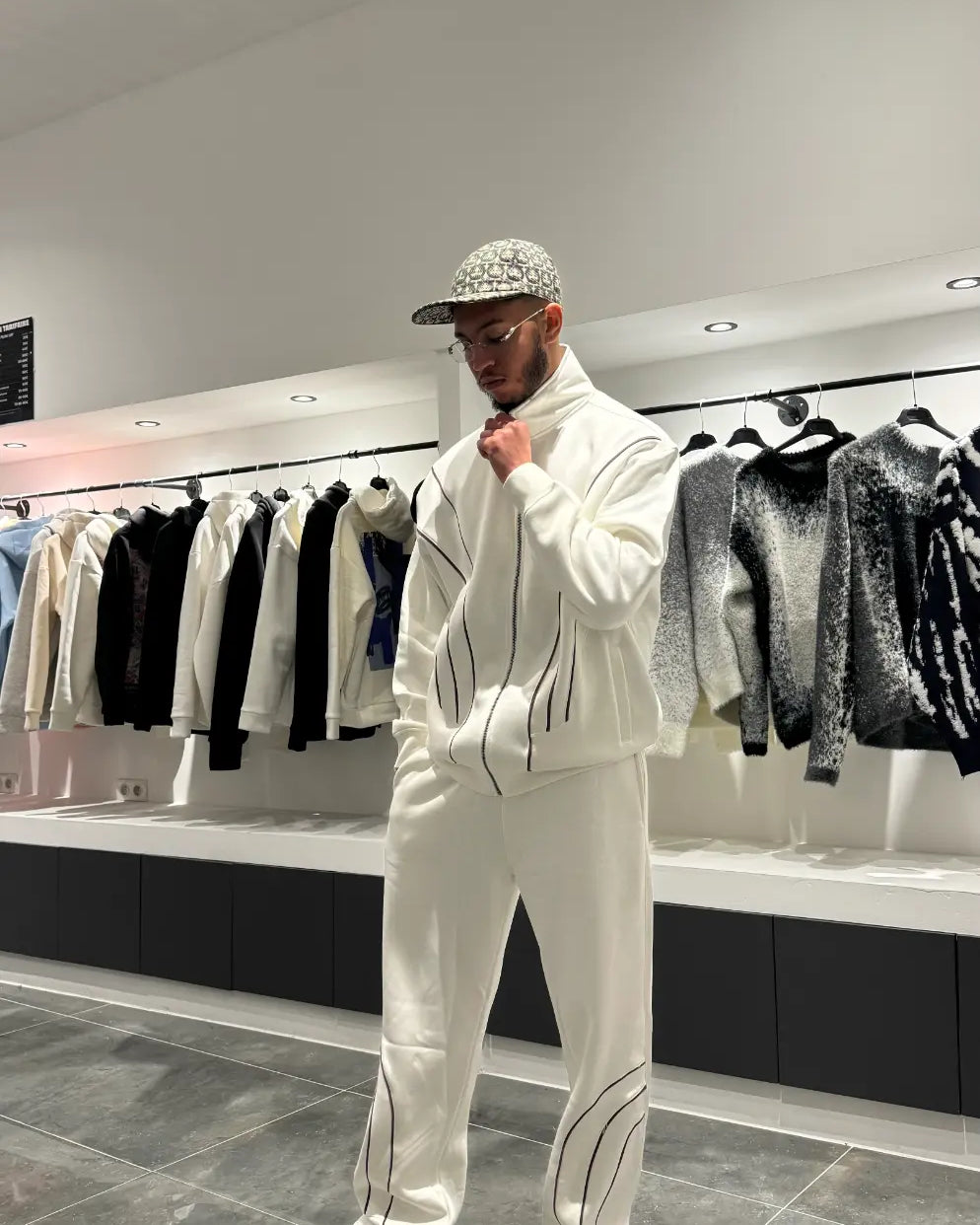 Ensemble blanc oversize composé d'une veste zippée sans capuche et d'un pantalon large, mettant en avant la ligne noire fine sur la poitrine.
