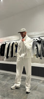 Ensemble blanc oversize composé d'une veste zippée sans capuche et d'un pantalon large, mettant en avant la ligne noire fine sur la poitrine.