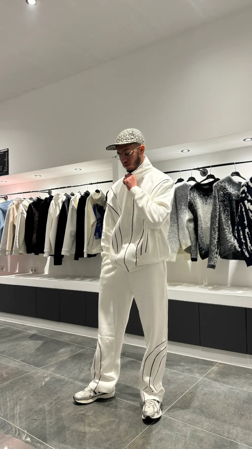 Ensemble blanc oversize composé d'une veste zippée sans capuche et d'un pantalon large, mettant en avant la ligne noire fine sur la poitrine.
