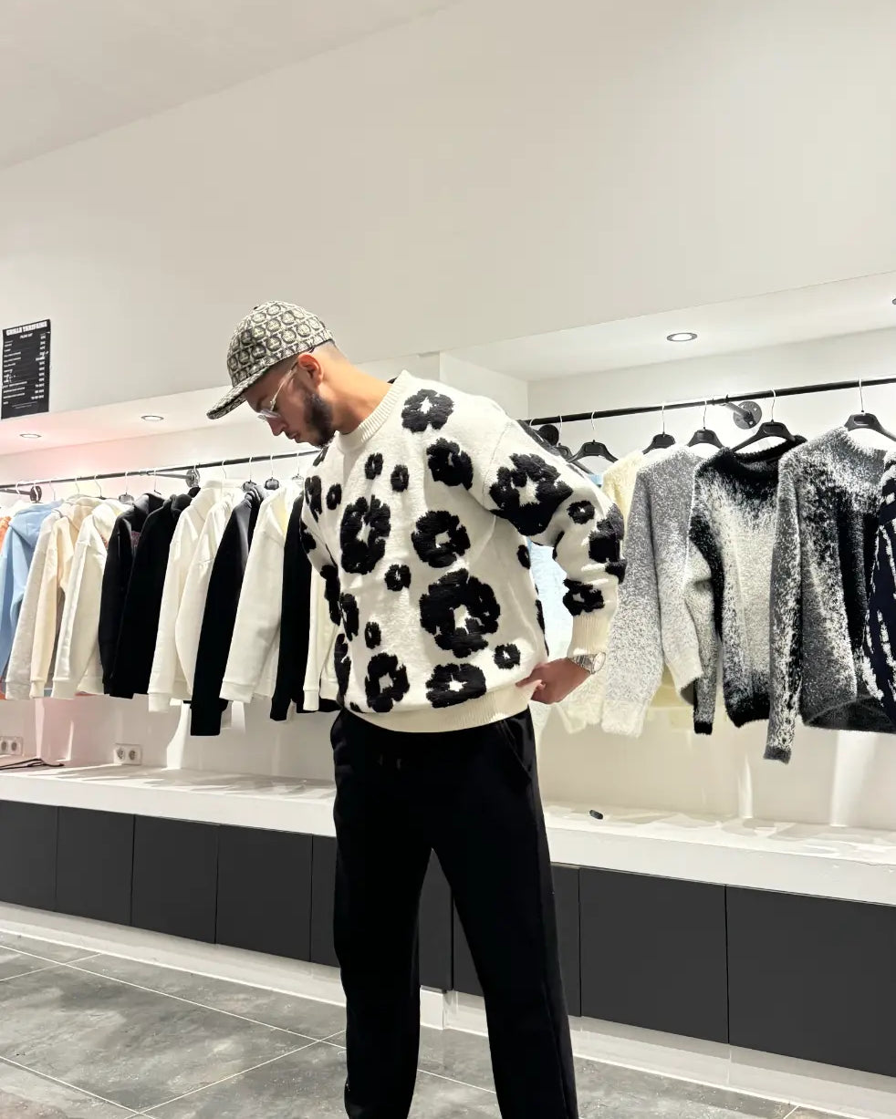 Pull en maille blanc oversize avec larges broderies florales noires sur le torse, porté dans un décor urbain.