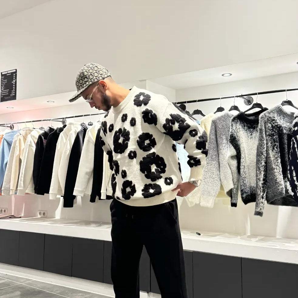Pull en maille blanc oversize avec larges broderies florales noires sur le torse, porté dans un décor urbain.