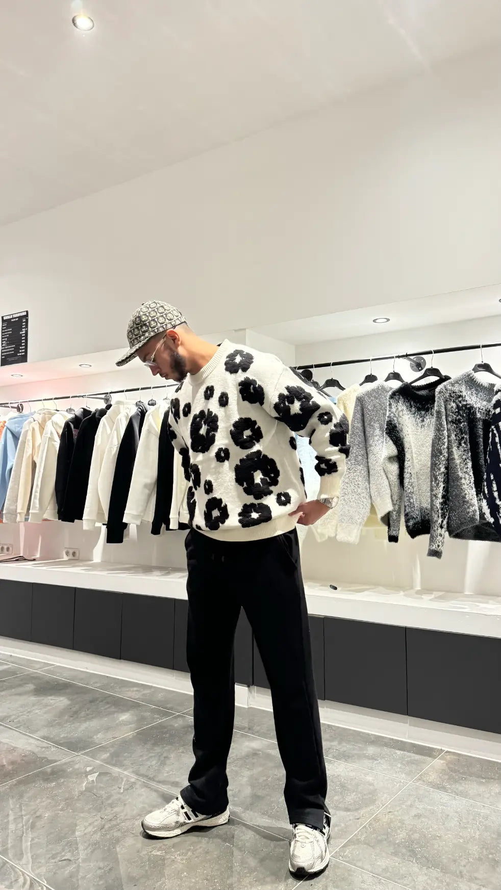 Pull en maille blanc oversize avec larges broderies florales noires sur le torse, porté dans un décor urbain.
