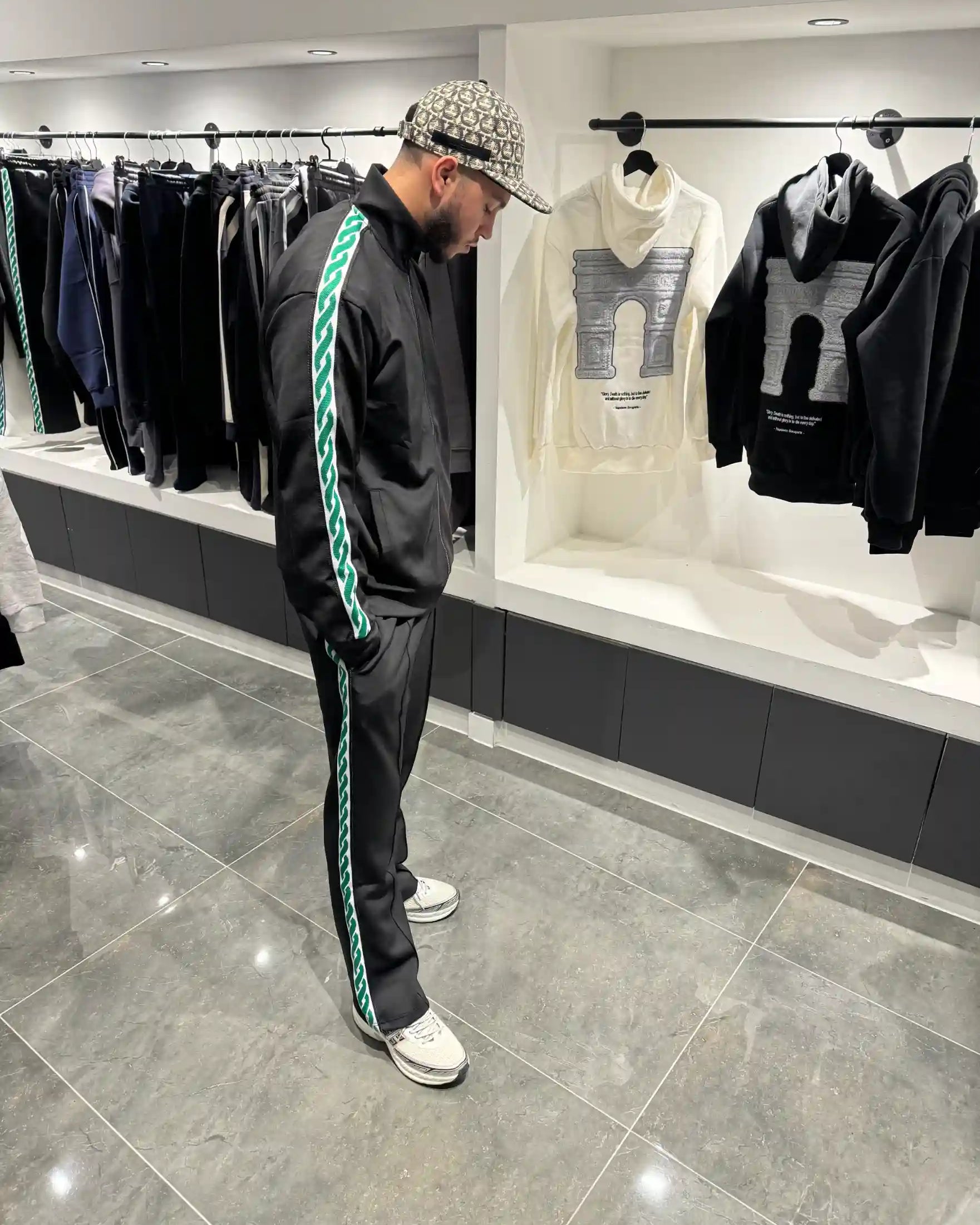 Silhouette complète montrant l'ensemble noir et les bandes de motifs verts distinctives le long des manches et des jambes.
