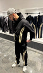 Ensemble streetwear noir avec veste zippée et jogging, présentant de larges bandes beiges verticales sur les bras et les jambes.