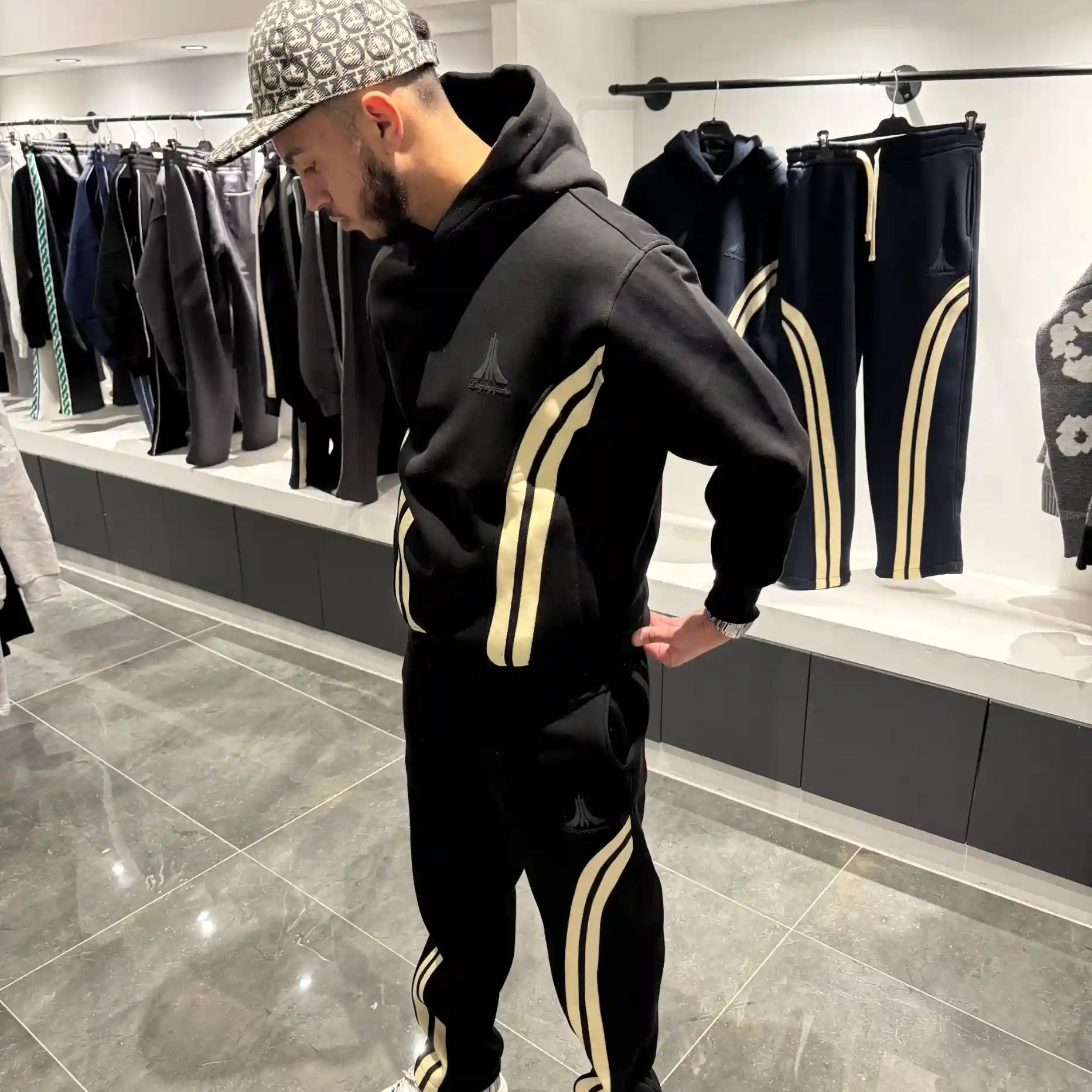 Ensemble streetwear noir avec veste zippée et jogging, présentant de larges bandes beiges verticales sur les bras et les jambes.