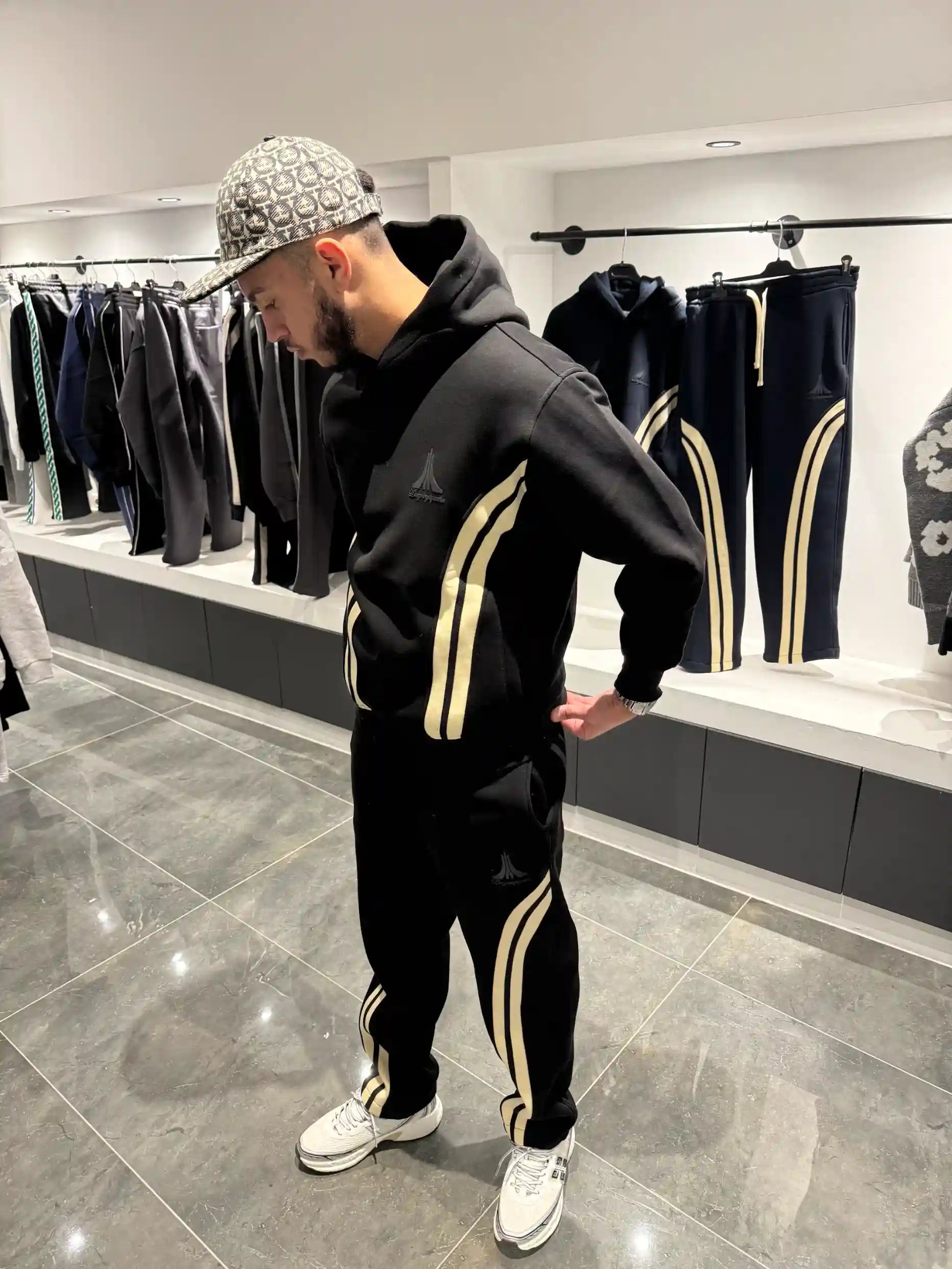 Ensemble streetwear noir avec veste zippée et jogging, présentant de larges bandes beiges verticales sur les bras et les jambes.