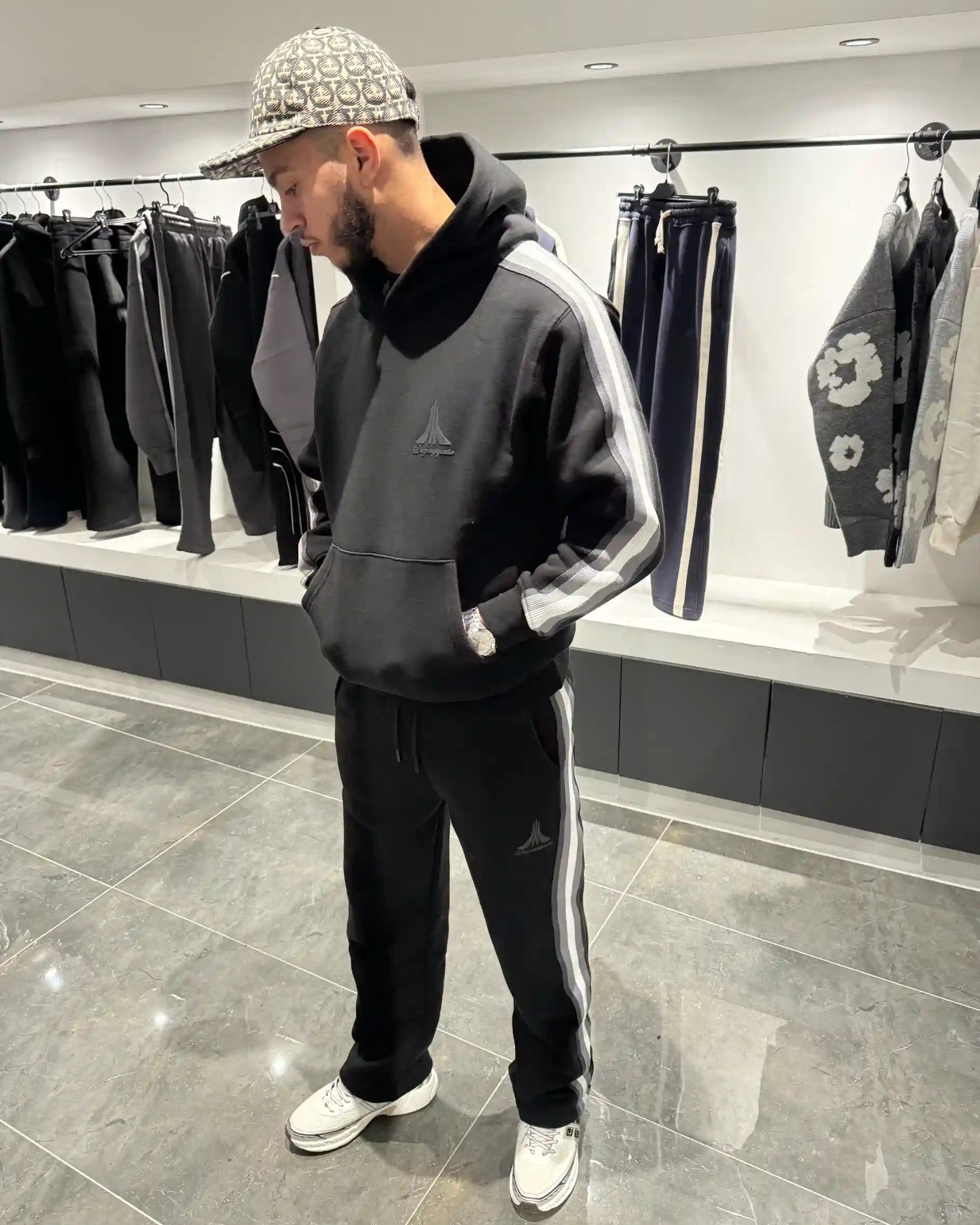 Silhouette complète présentant l'ensemble noir avec le hoodie et le contraste des larges bandes beiges sur les côtés.