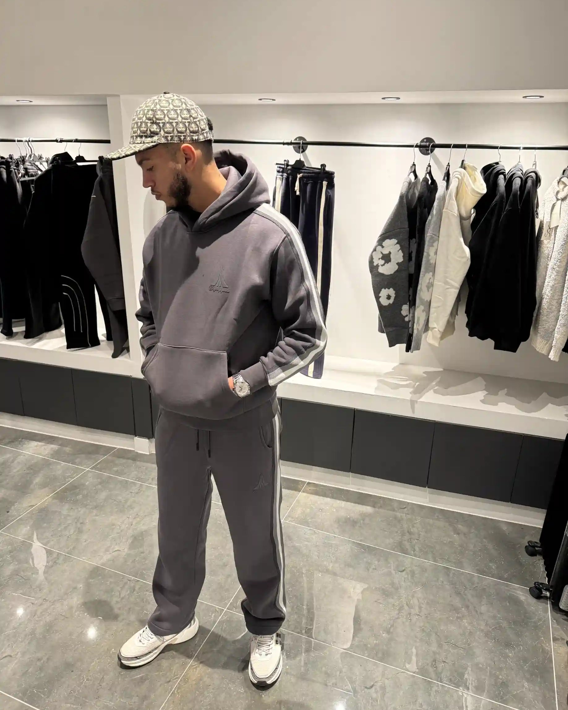 Silhouette complète présentant l'ensemble gris avec le hoodie et l'impact visuel des larges bandes beiges sur les côtés.