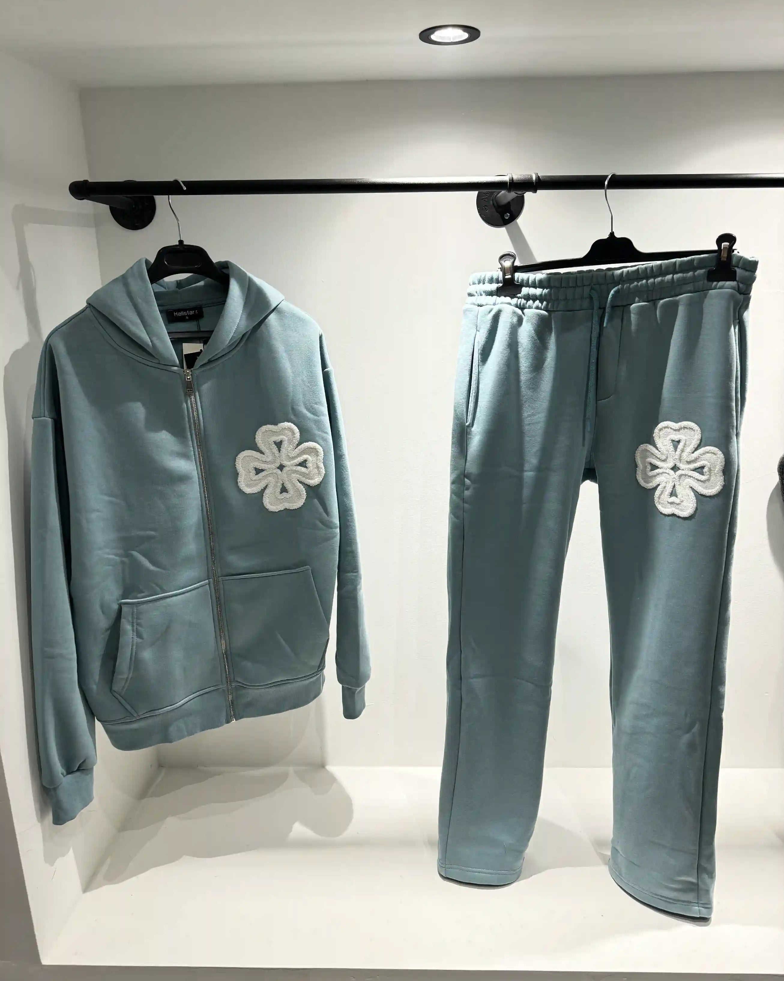 Présentation de l'ensemble bleu clair sur cintre, illustrant la fluidité du textile et le design des trèfles blancs.