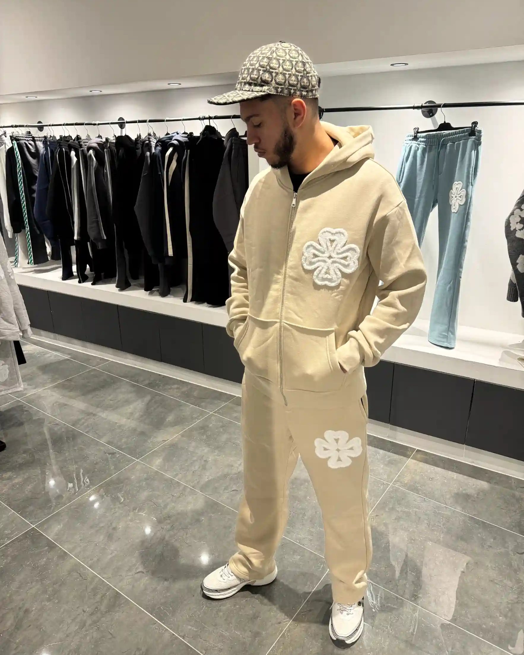 Silhouette complète présentant l'ensemble beige et l'impact visuel des trèfles blancs.